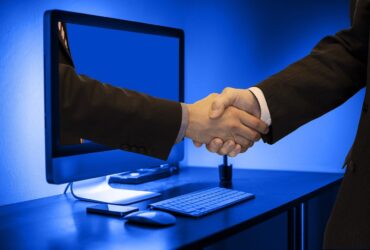 デスクトップパソコンの前で握手するビジネスマンの腕